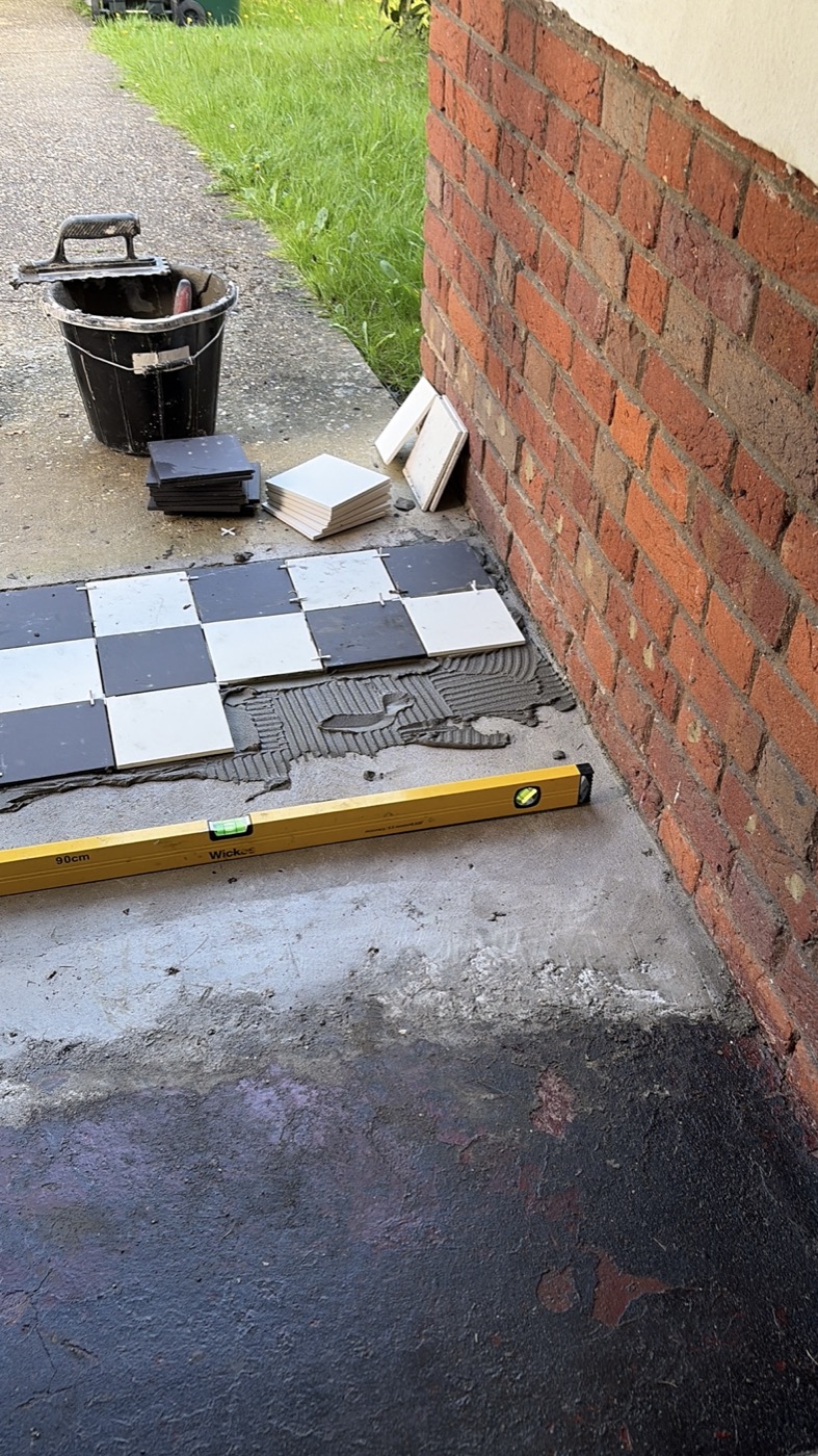 Black and white checkerboard porch tiles being laid — adhesive and spacers visible